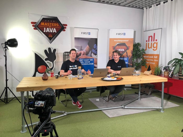 Twee mensen achter een tafel met ICT posters op achtergrond