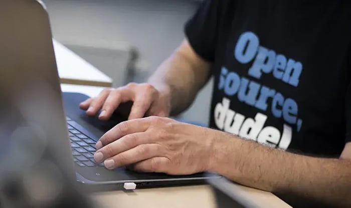 Man typt op laptop en draagt shirt met: Open Source Dude!