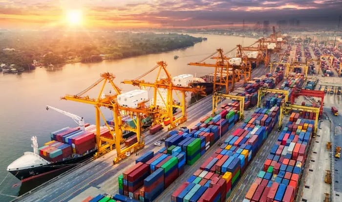 Container terminal with cranes loading cargo ships at a port during sunset.