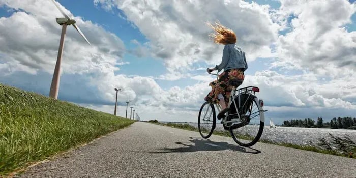 Vrouw fietst op een dijk en haar haren vliegen in de wind.