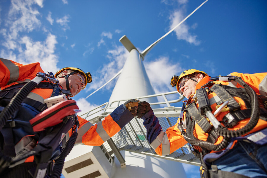 Two gentlemen from Eneco give each other a fist-bump under a windmill