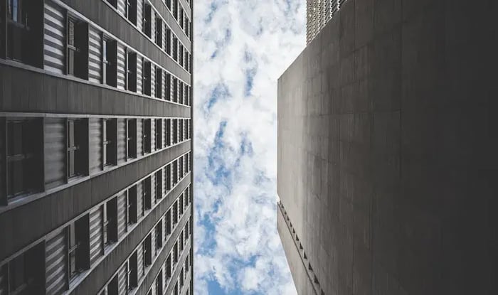 View looking up between modern office buildings toward a cloudy sky.