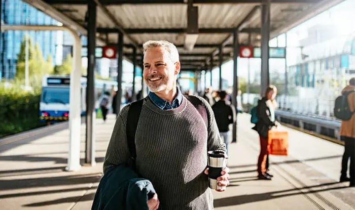 Man wacht glimlachend op het perron met een koffiebeker in zijn hand.