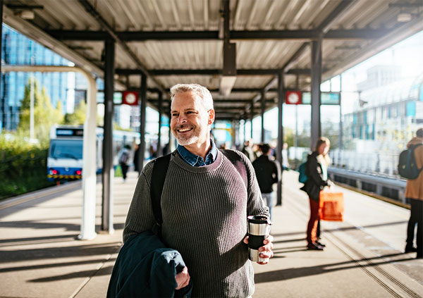 een lachende man op het station met koffie in zijn hand