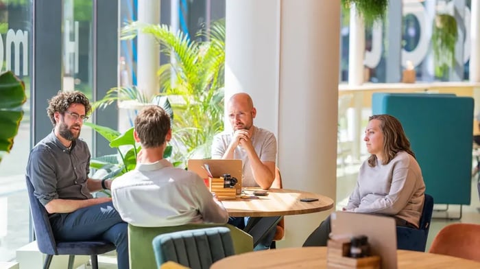 Vier mensen in gesprek rondom een tafel in een informele maar zakelijke setting