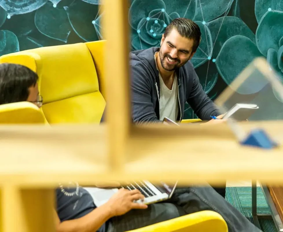 wee mannen zitten in een gele fauteuil en lachen terwijl ze werken op laptops en tablets