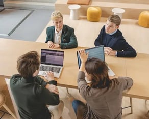Vier collega's aan een houten bureau met twee laptops.