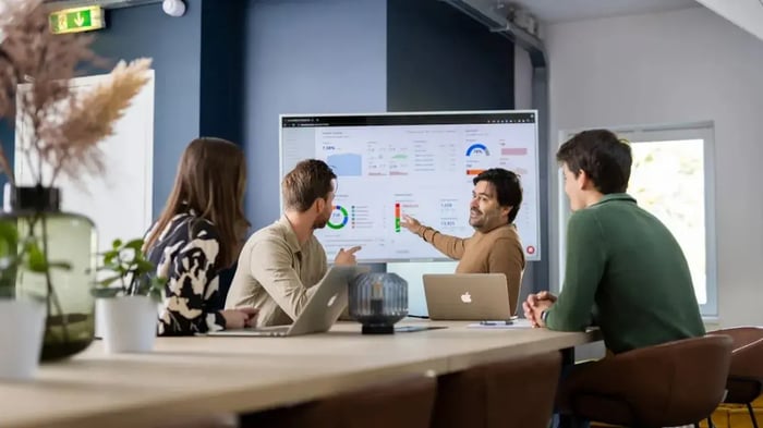 Collega's in een vergaderruimte wijzen naar een scherm.