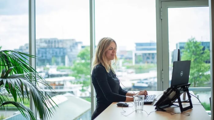 Vrouw staat achter haar bureau en kijkt naar haar laptop.