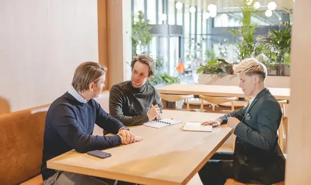 Drie collega's zitten aan een houten bureau met hun notitieboekjes.