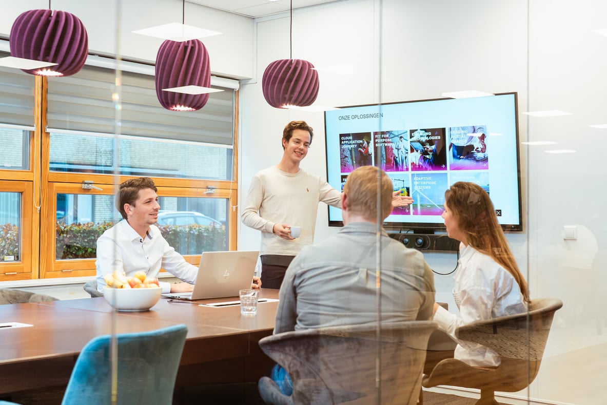 Medewerker staat in een vergaderzaal en presenteert aan zijn collega's