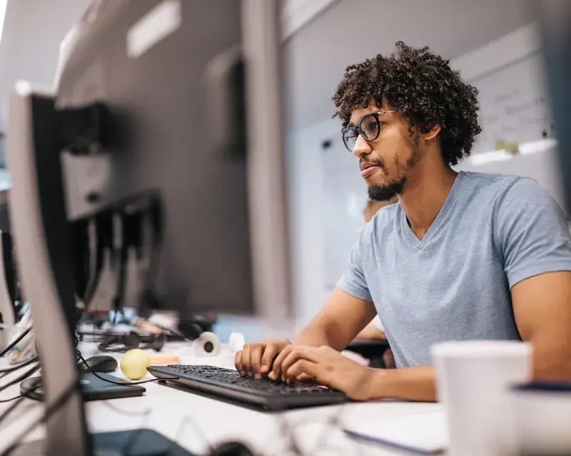 Man in grijs t-shirt en met donker krullend haar die typt op toetsenboard