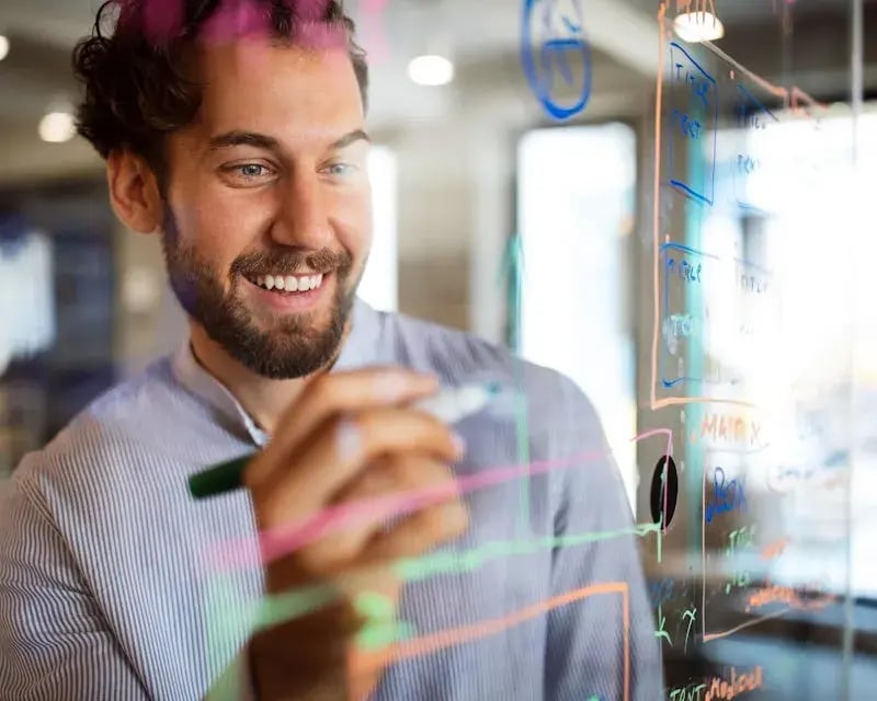 Jonge man schrijft met gekleurde stiften op een glazen wand