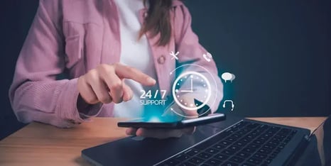 Persoon die met een vinger een smartphone bedient naast een laptop, met een digitale overlay van een klok en pictogrammen die 24/7 online support visualiseren.