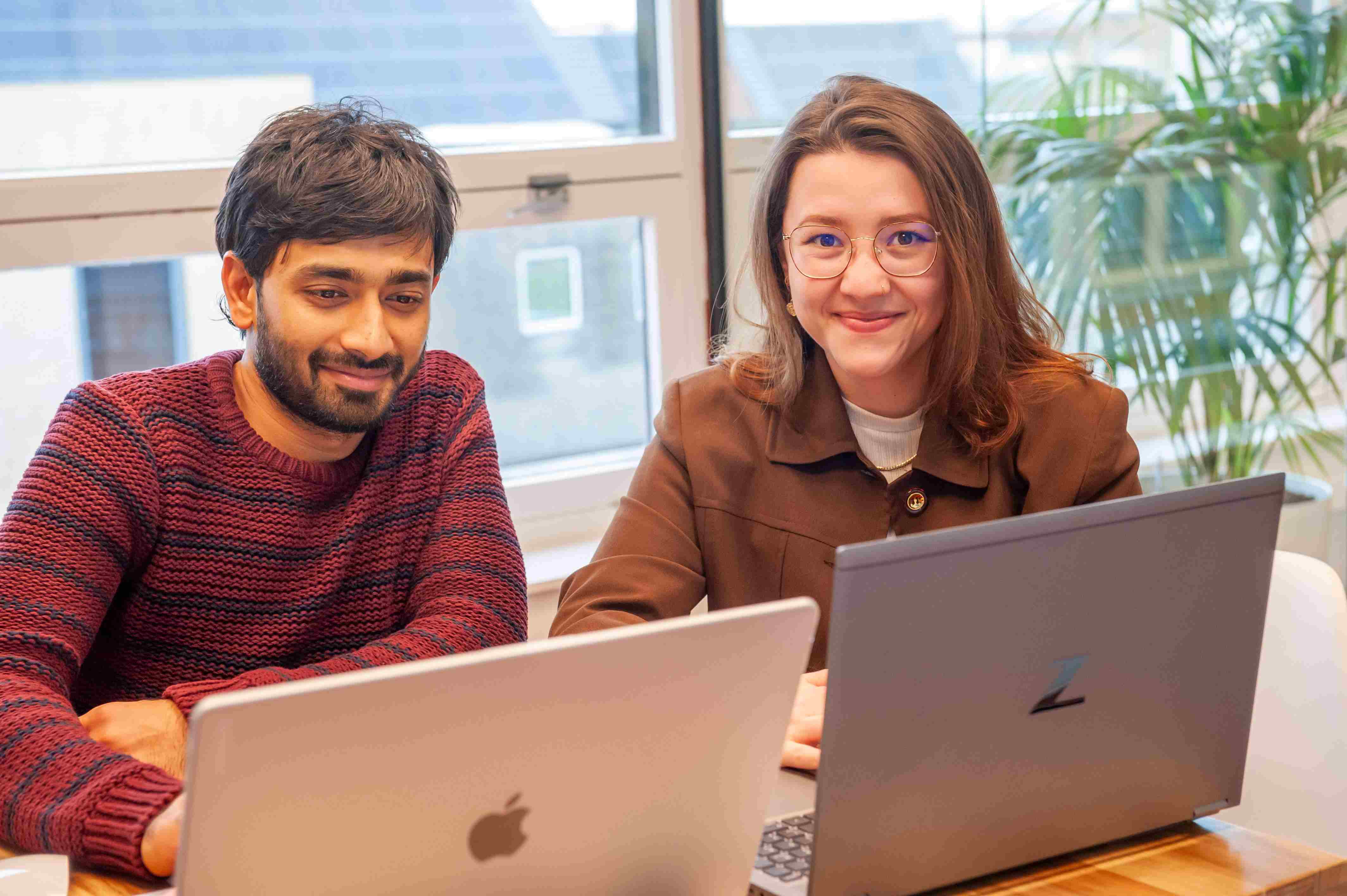 Man and woman smiling and working on laptops in an office.