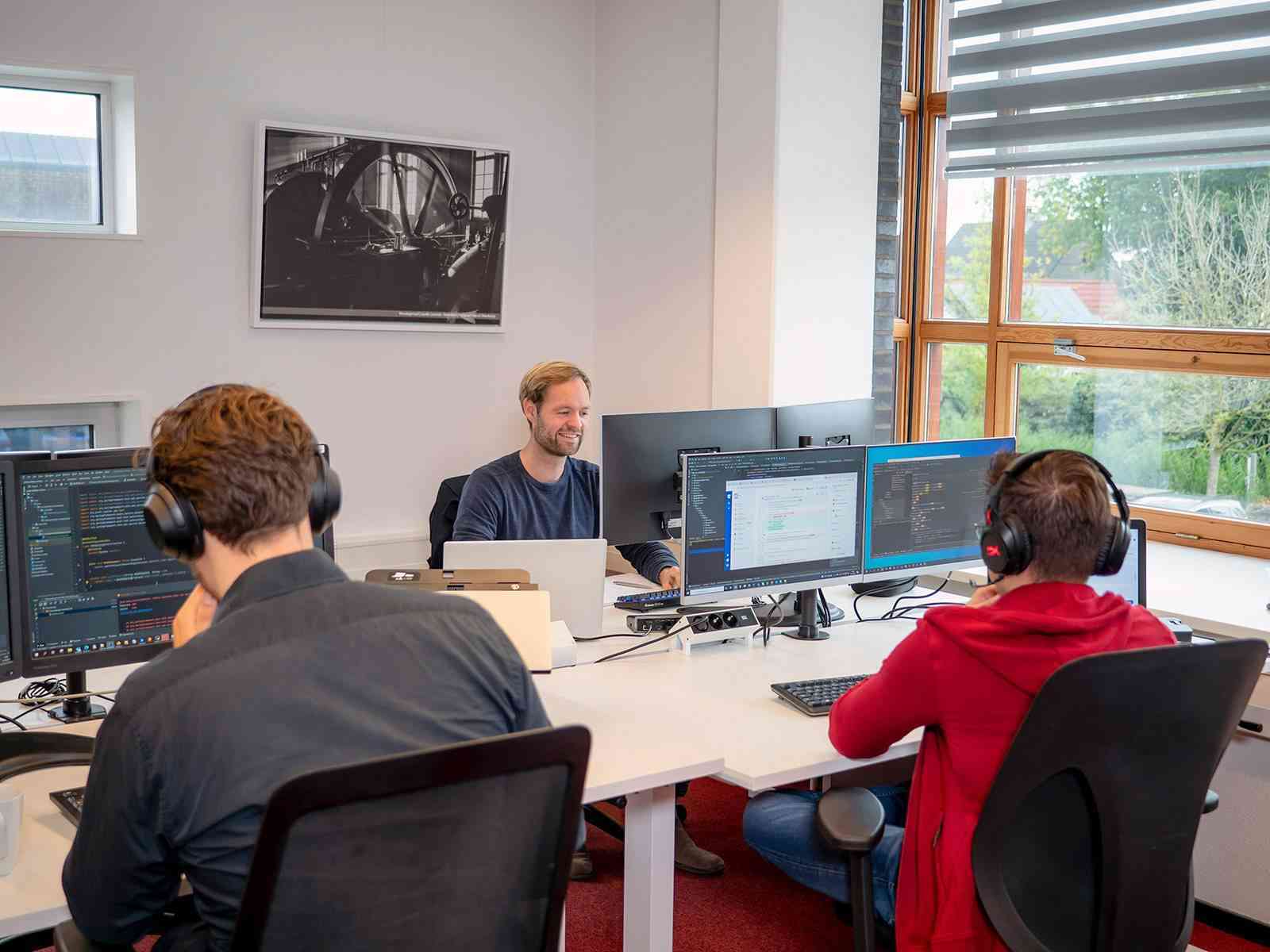 Two people work concentratedly behind multiple monitors in an office.