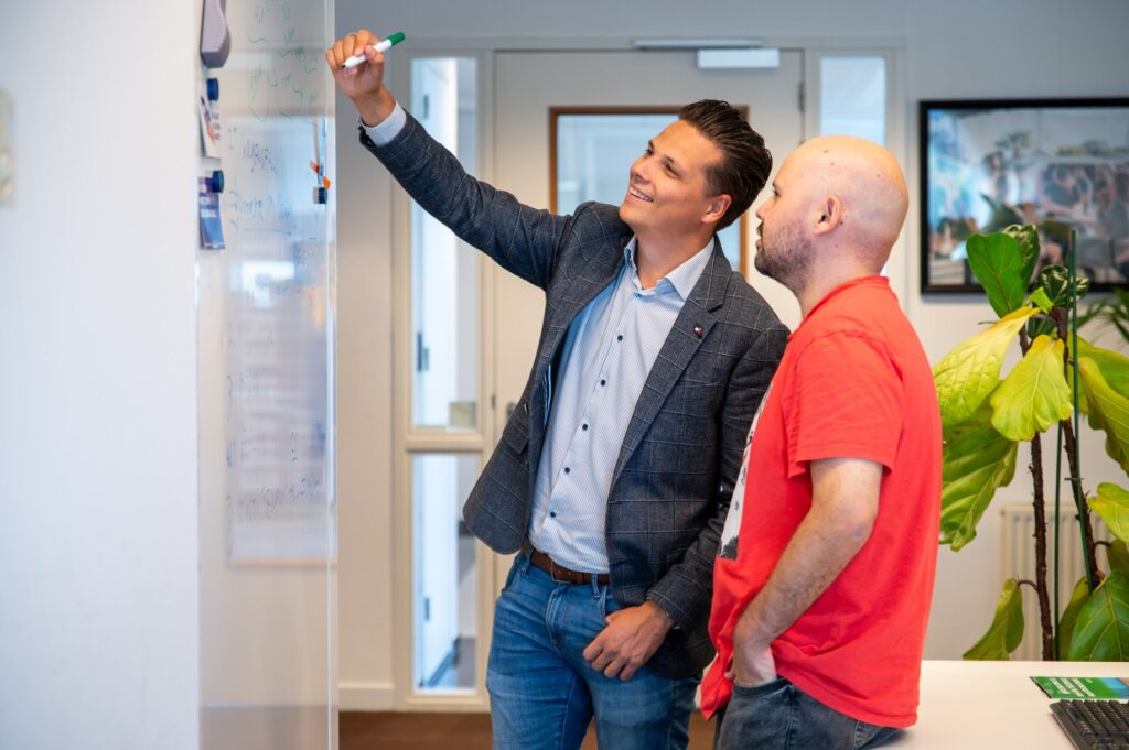 Twee mensen bespreken iets op een whiteboard in een kantoor.