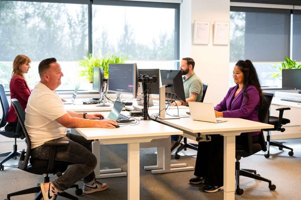 Vier mensen werken aan bureaus in een moderne kantoorruimte.