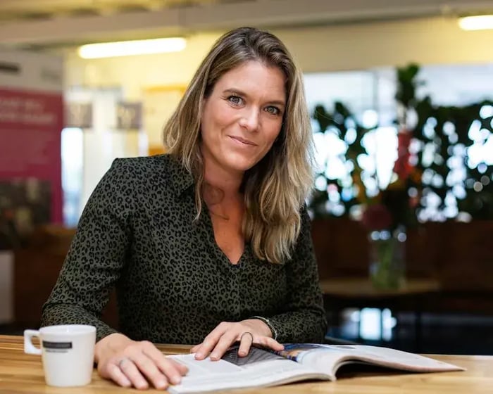 Een dame met een boek en een kop koffie kijkt in de camera