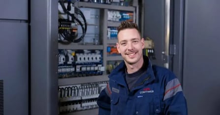 Man in bedrijfskleding Contiweb staat voor servers en lacht