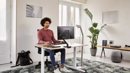 landscapexl-ahrend-home-hvm-desk-in-white-with-oak-tabletop-and-black-ease-office-chair-with-grey-recharge-and-pyramid-bench-with-male-model-thinking-in-a-work-from-home-set-1