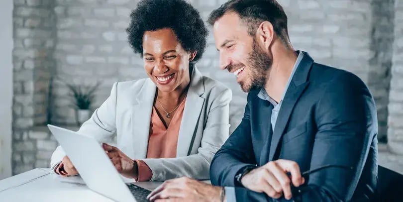en man en een vrouw in zakelijke kleding kijken samen naar een laptopscherm