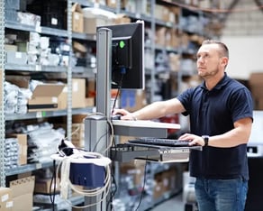 Medewerker in magazijn kijkt op een computer met op de achtergrond volle schappen