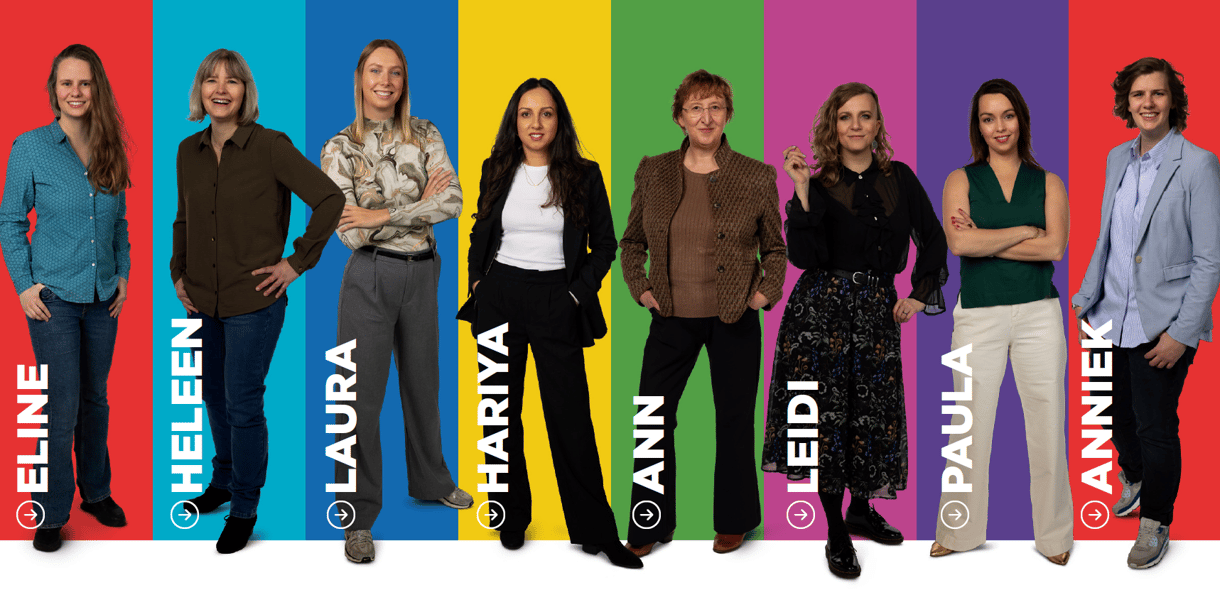 8 vrouwen die tegen een gekleurde achtergrond staan en lachen en met armen in zij of over elkaar in de camera kijken