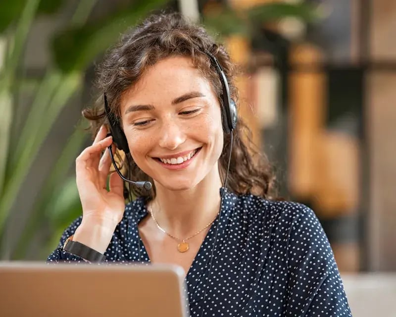 Lachende vrouw met headset in zakelijke omgeving achter haar laptop