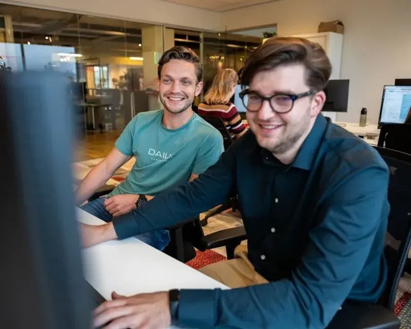 Twee jonge, mannelijke medewerkers die samen naar een computerscherm kijken