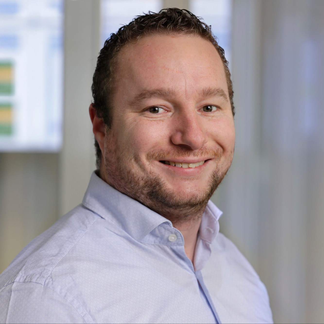 Mannelijke collega kijkt vriendelijk de camera in.