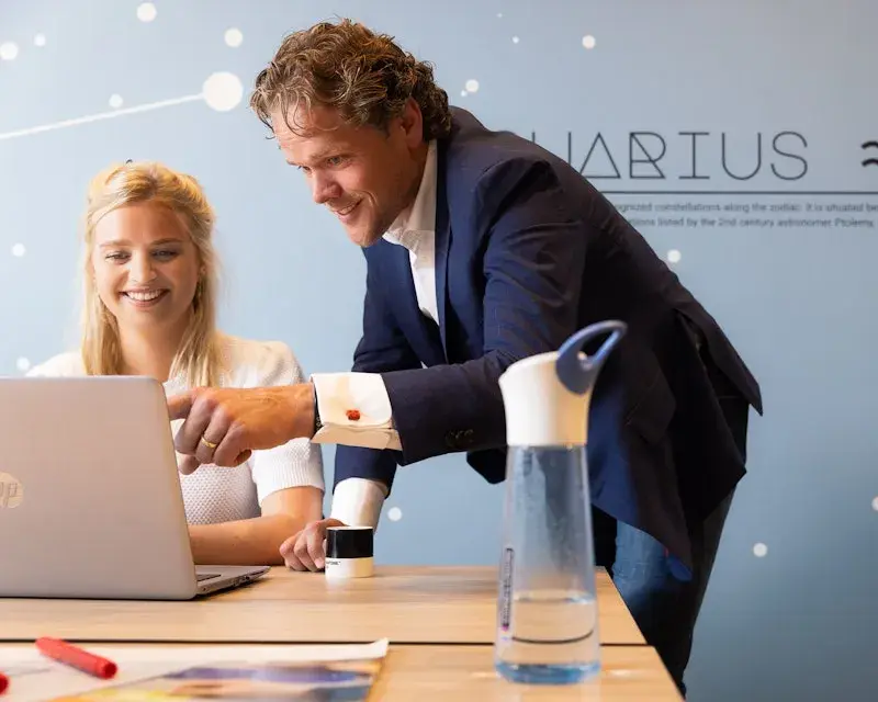 Man leunt op bureau en wijst naar de laptop van zijn collega.