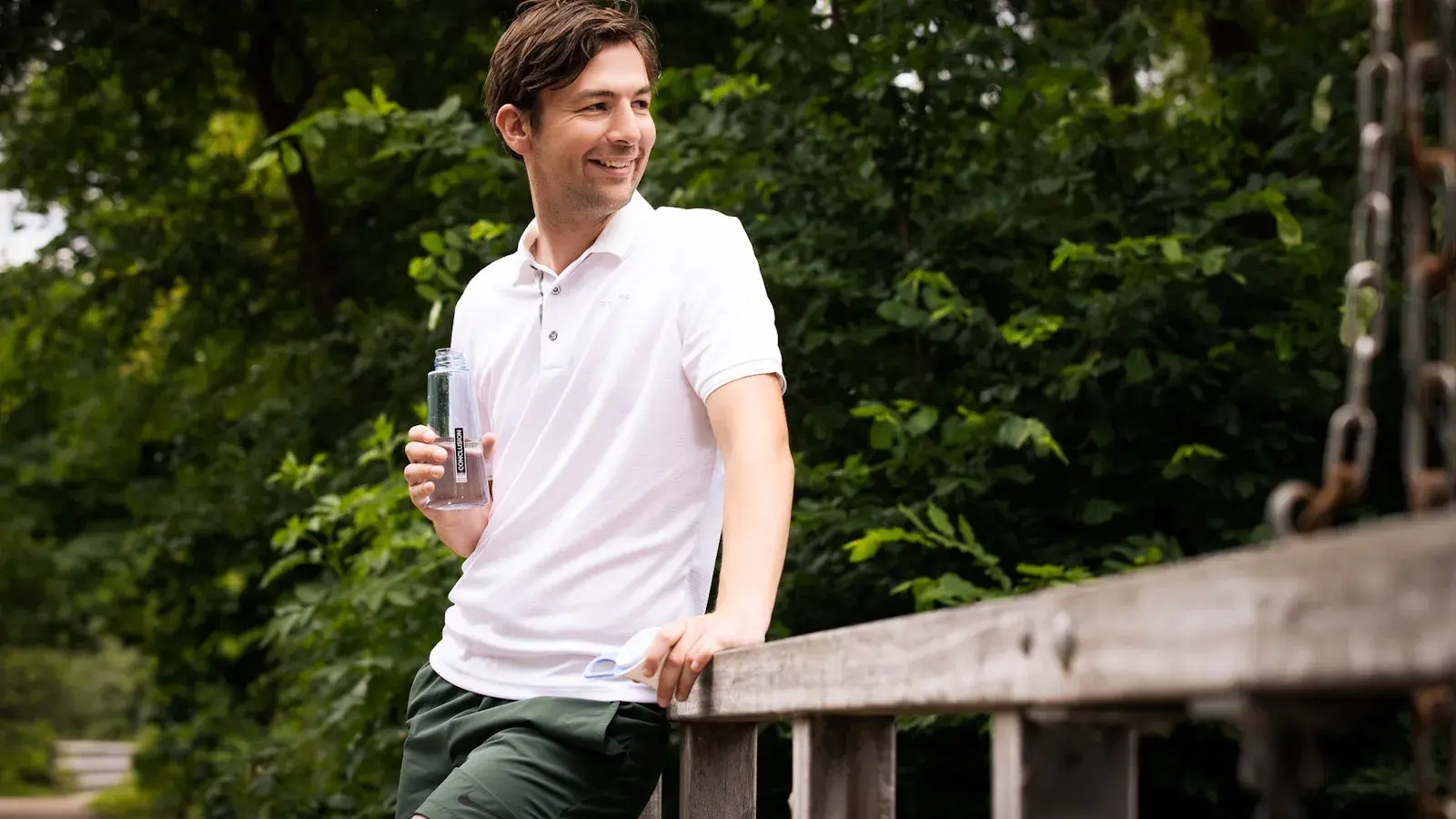 Man leunt tegen een bruggetje aan met Conclusion waterfles in zijn hand.