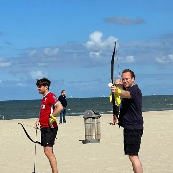 Twee mannen op het strand die boogschieten