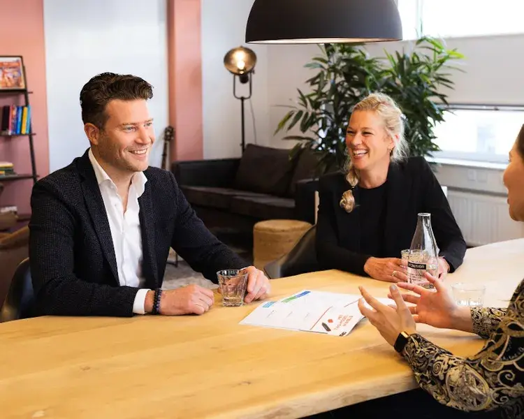 Collega's zitten aan tafel en lachen met elkaar.