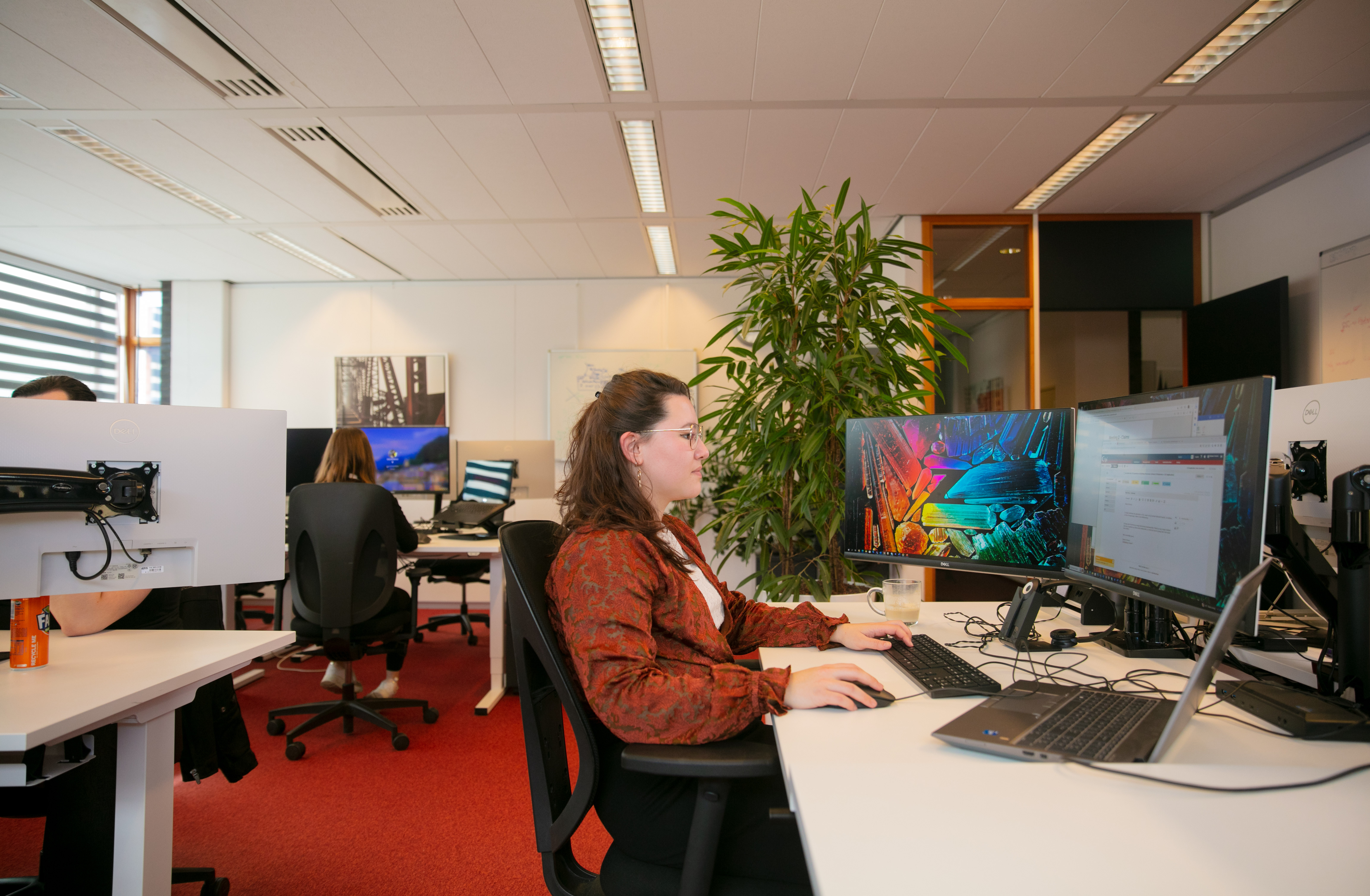 Een vrouw werkt achter een computer op een modern kantoor met meerdere beeldschermen.