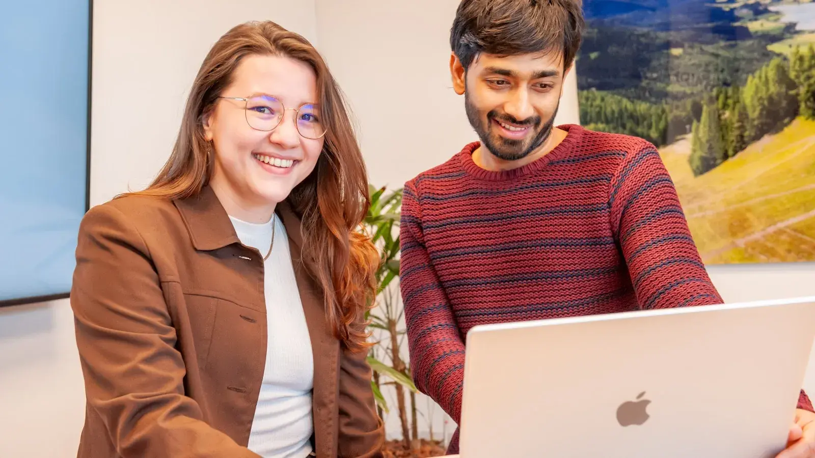 A female and male colleague are looking at a laptop and laughing.