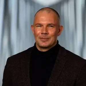 Mannelijke collega in nette zwarte kleding kijkt vriendelijk de camera in.