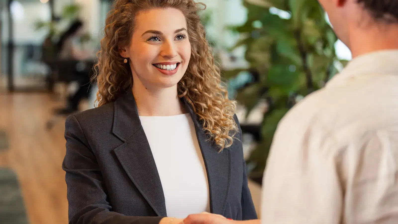 Vrouw schudt de hand van een man en lacht vriendelijk.