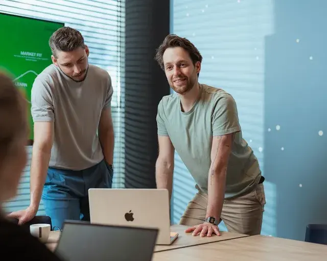 Twee collega's leunen over hun laptop op tafel.