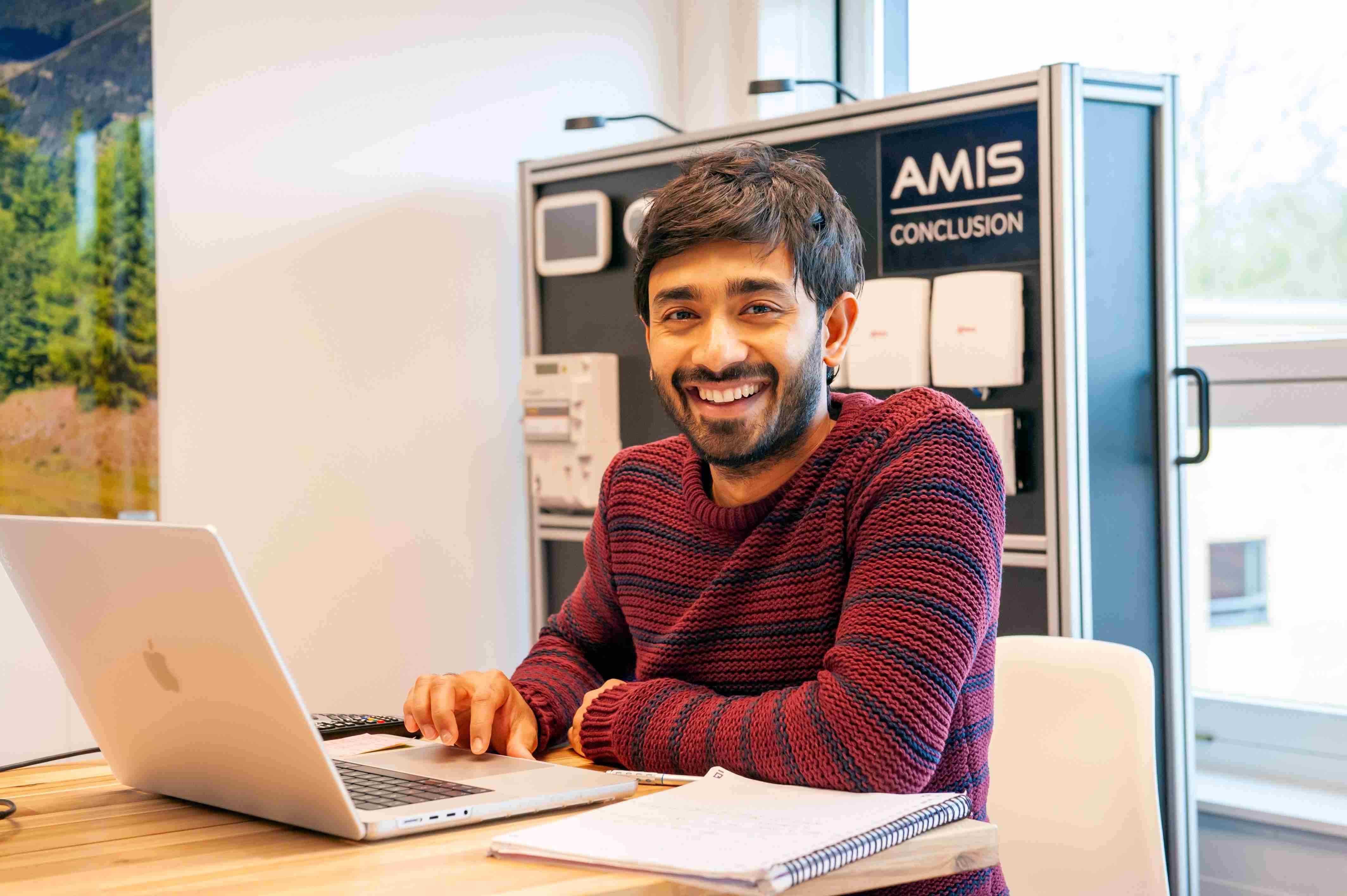 Man in sweater smiles while working on his laptop