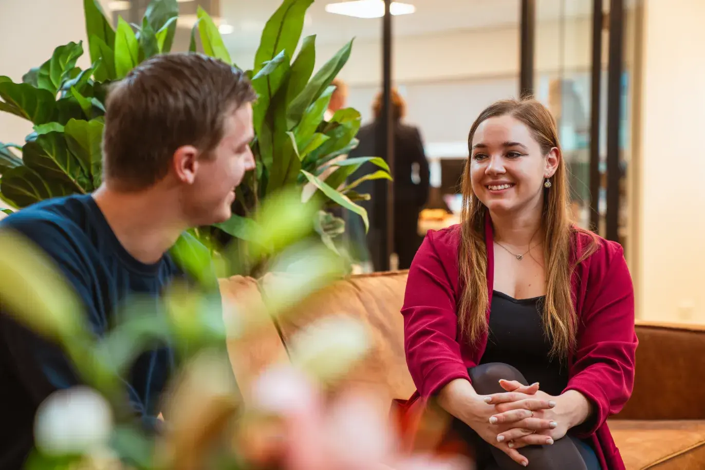 Twee jonge collega's op een bruine bank op kantoor in gesprek