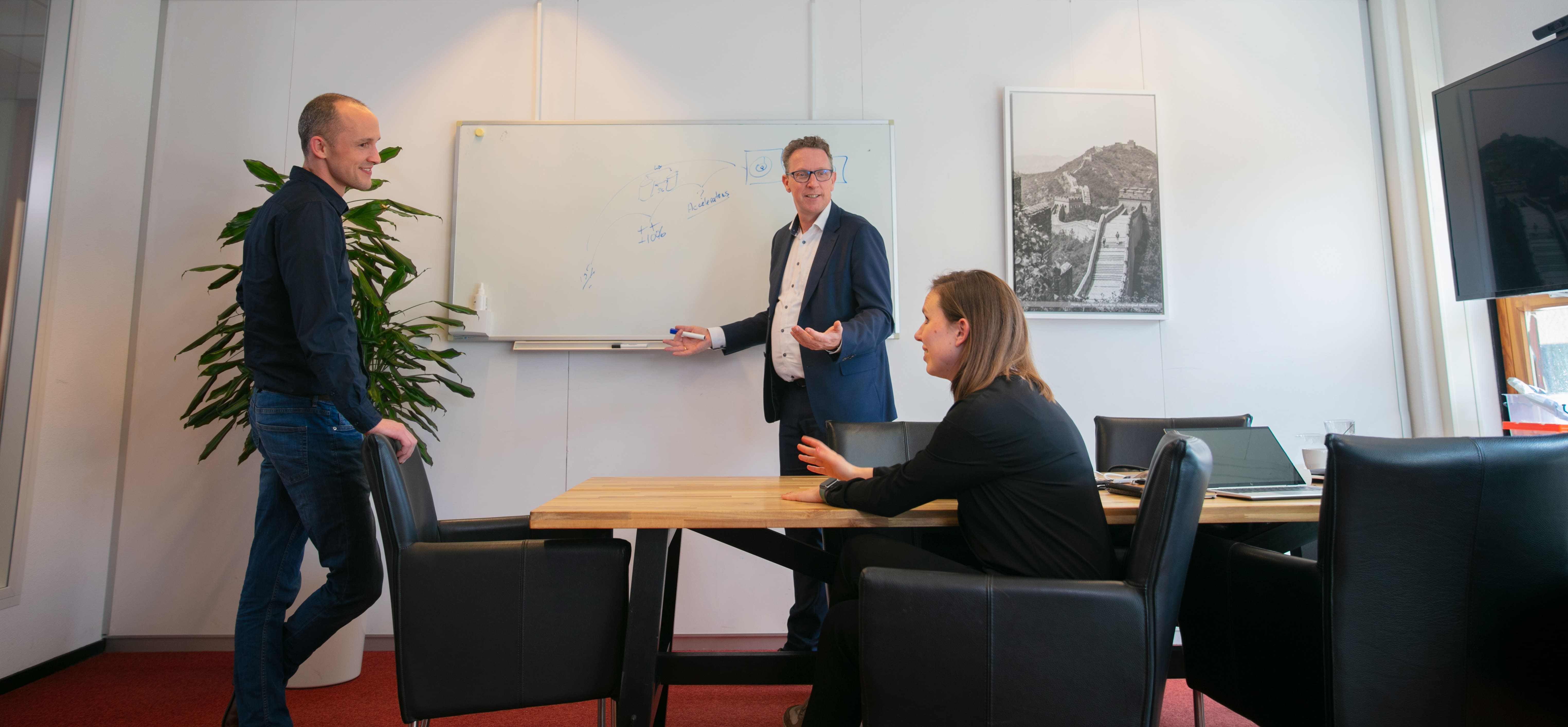 Three colleagues in a meeting room discussing.