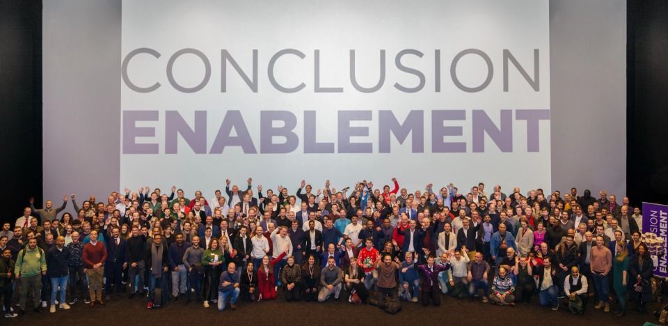 Groep mensen poseert samen voor een foto met het 'CONCLUSION ENABLEMENT' logo op de achtergrond.