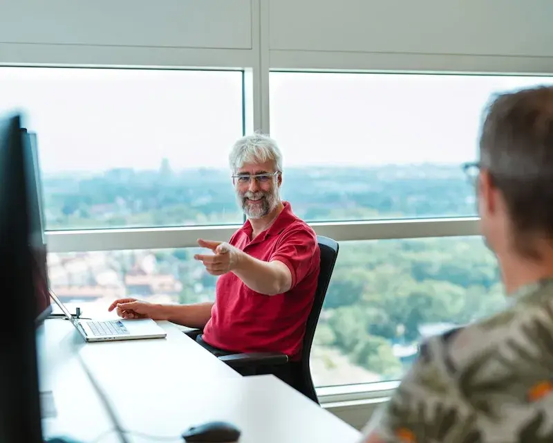 Twee collegas aan het werk, eentje wijst naar een scherm