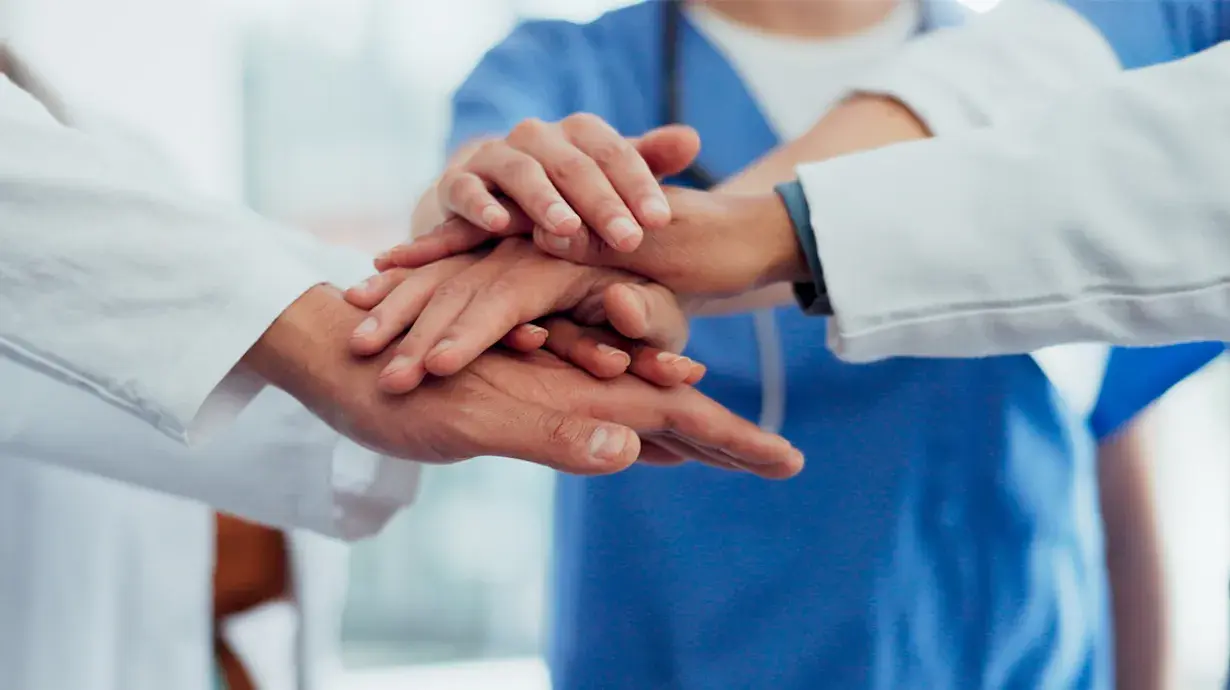 Meerdere paren handen van dokters en verpleegkundiger op elkaar.